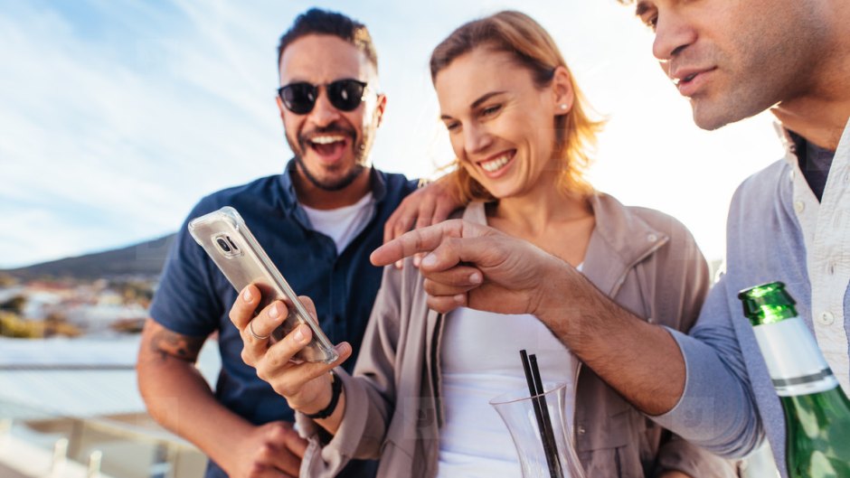 a bunch of people on the beach looking at a cell phone