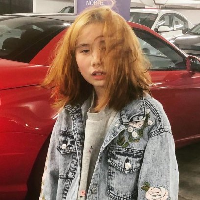 A picture of Lil Tay standing in front of a red car