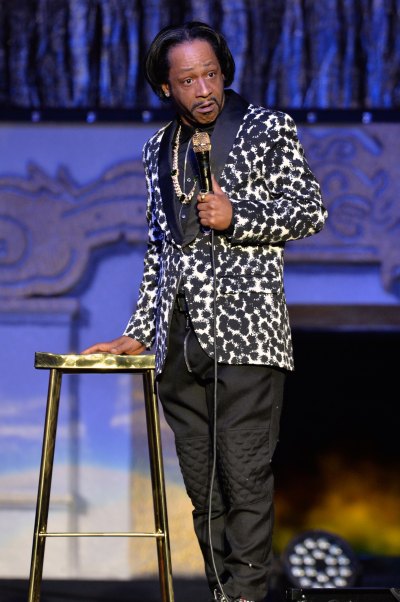 Katt Williams holds a mic while wearing a black and white jacket on stage.